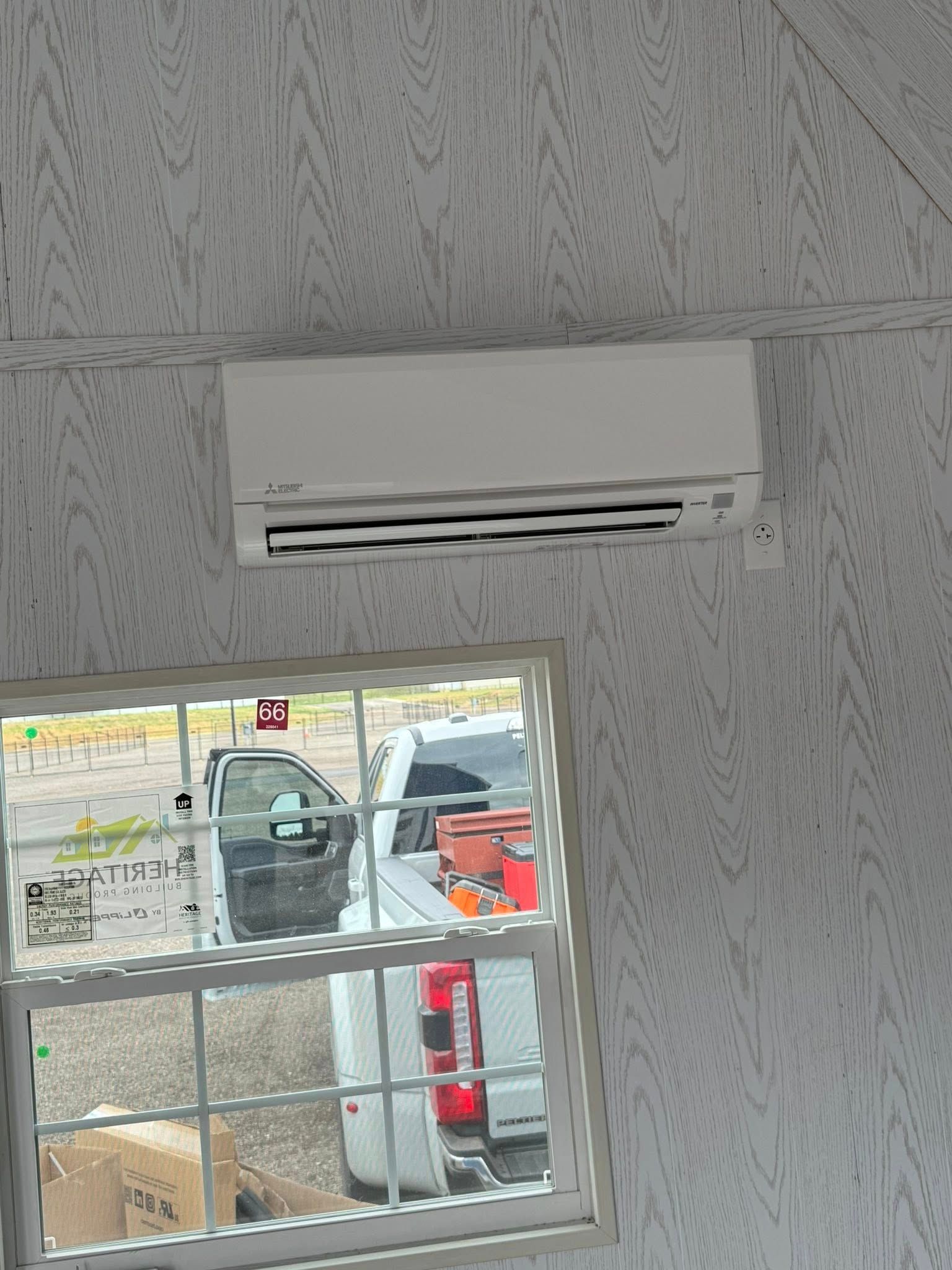 White air conditioner above a window, set in a light-colored, wood-grain interior. Cars are visible outside.