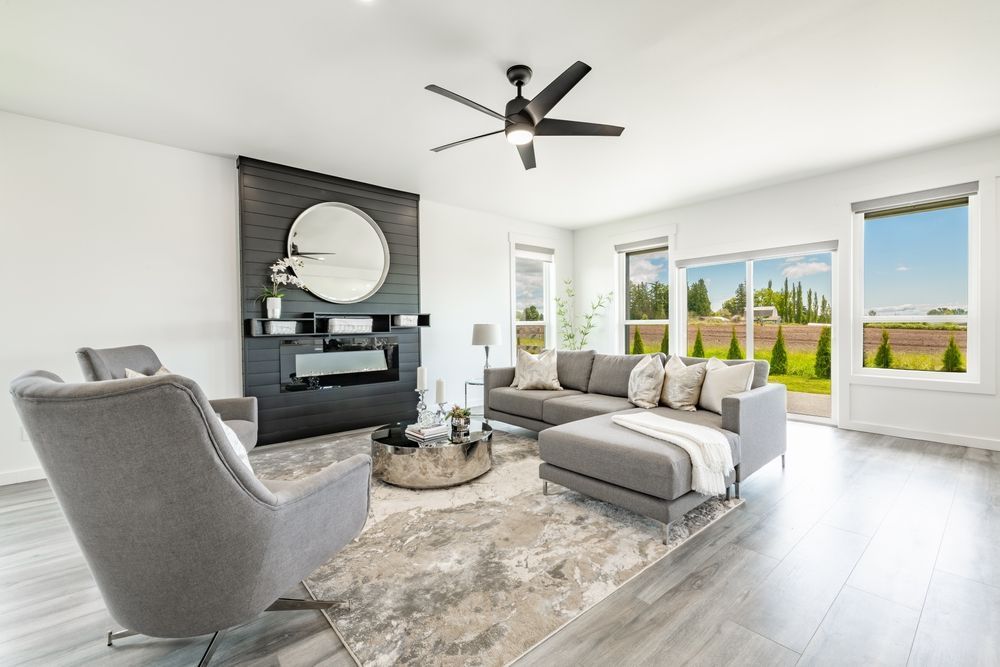 Modern living room with grey furniture, fireplace, large mirror, and view of landscape through window.