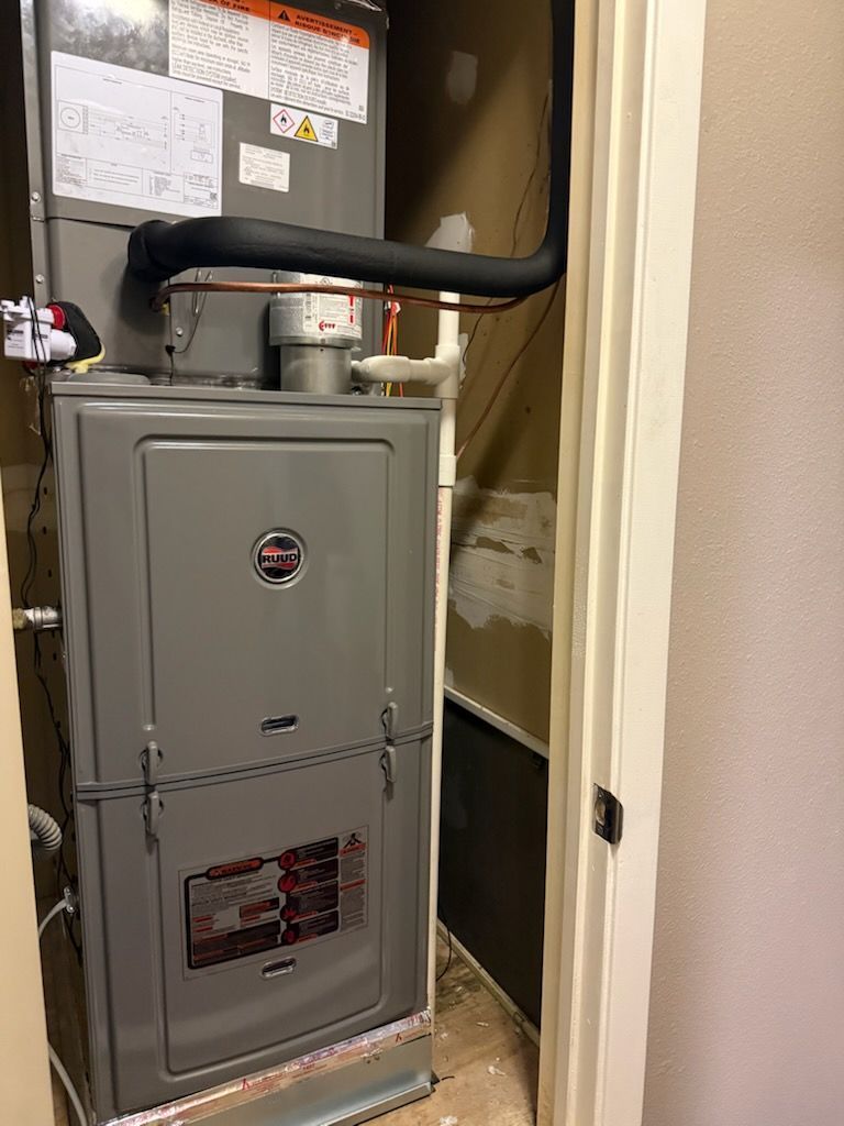 Furnace unit in a closet. Gray metal with ductwork, piping and electrical connections visible.