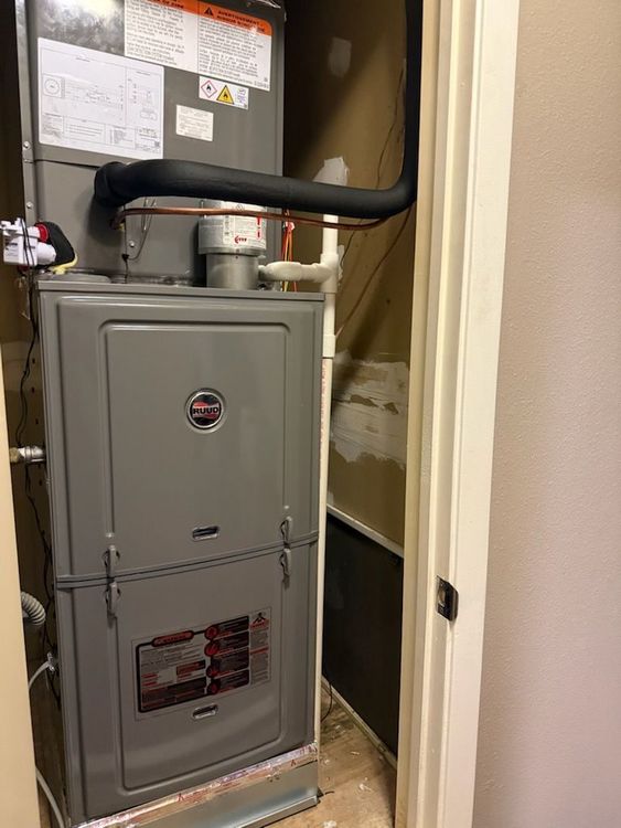 Furnace unit in a closet. Gray metal with ductwork, piping and electrical connections visible.