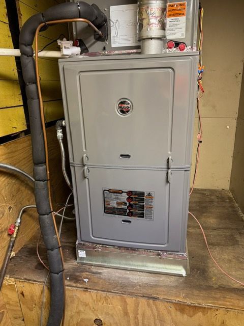 Gray furnace in a wooden enclosure with black insulated pipes.