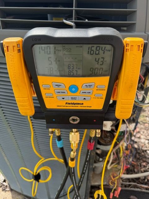 Yellow and black digital HVAC manifold gauges attached to an air conditioning unit; readings visible.