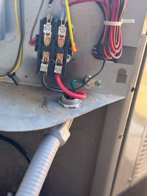 Close-up of an electrical box with wires connected to a contactor and grounding point in an outdoor unit.