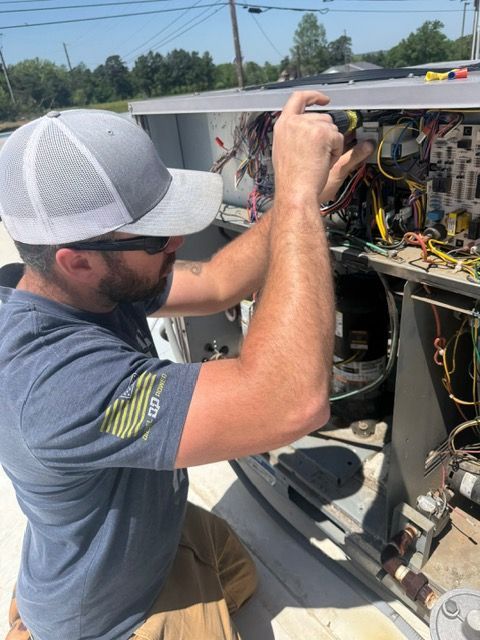 Man in gray cap and sunglasses repairs HVAC unit wiring outdoors.