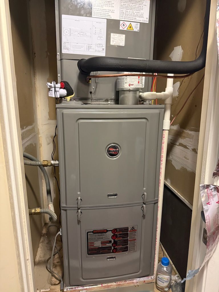 A gray furnace unit in a closet with pipes and a bottle of water on the floor.