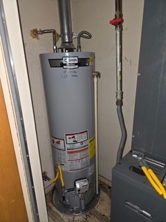 A grey A.O. Smith water heater in a closet, with visible plumbing connections, a vent pipe, and a nearby furnace unit.