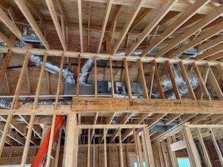 Unfinished wooden ceiling joists with exposed HVAC ductwork and a central air unit in a new construction home.