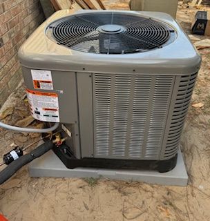 A gray outdoor residential HVAC condenser unit installed on a concrete pad next to a brick house.