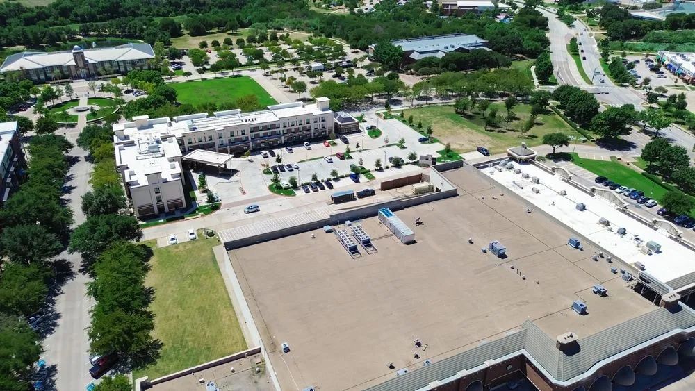 Aerial view of buildings, parking lots, and green spaces on a sunny day.