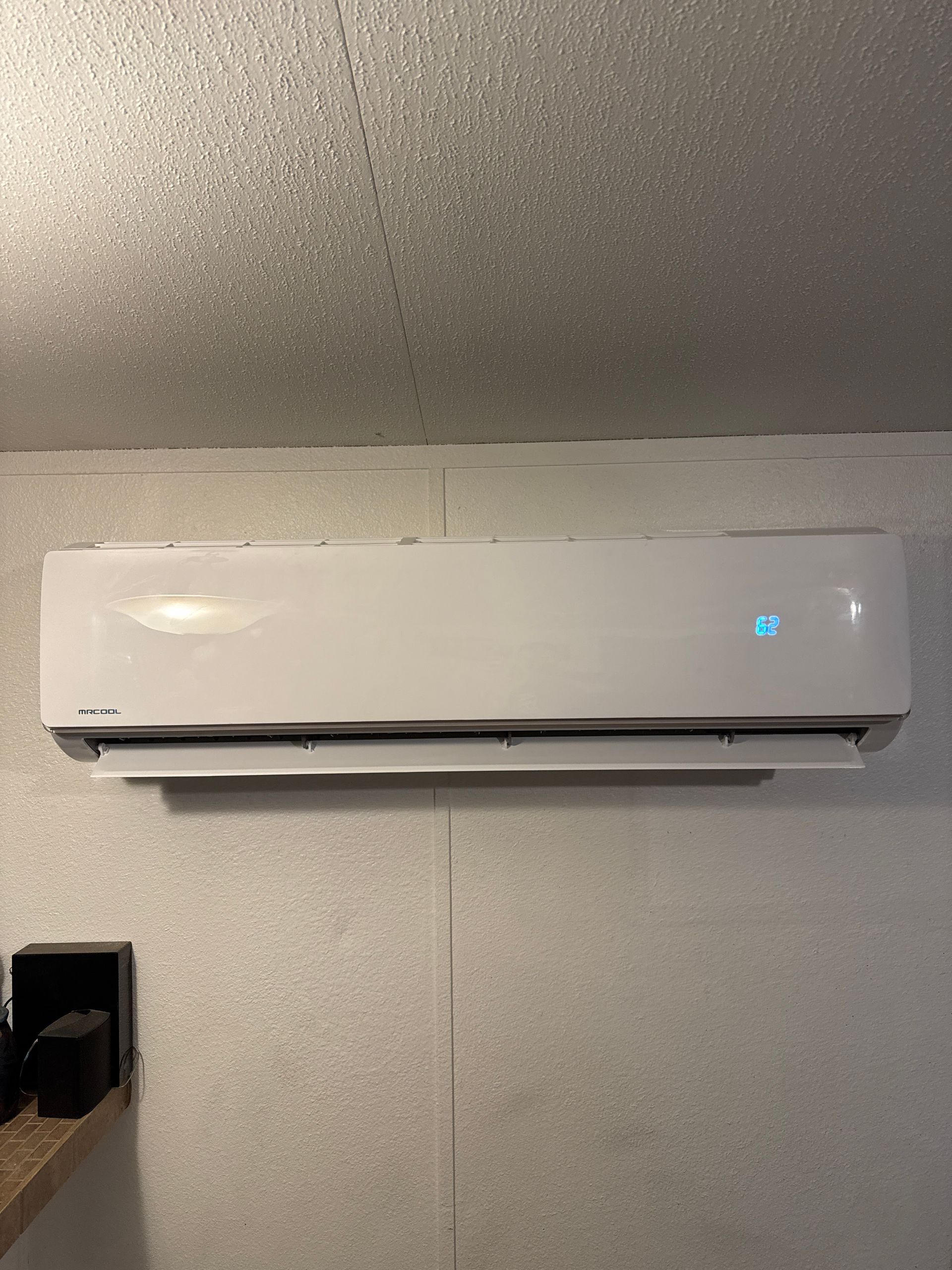 White wall-mounted air conditioner with a blue display against a white wall and ceiling.