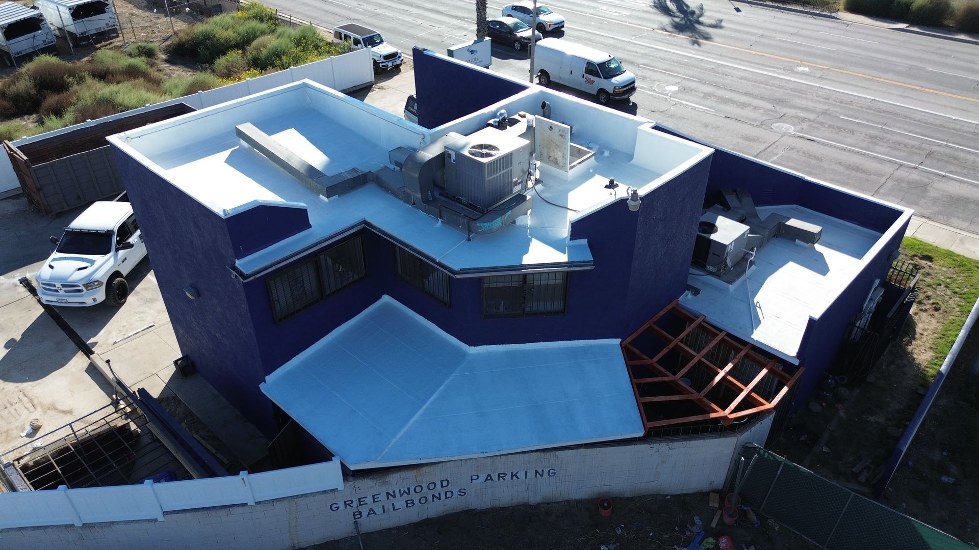Aerial view of a blue commercial building with a flat white roof. Vehicles are nearby.