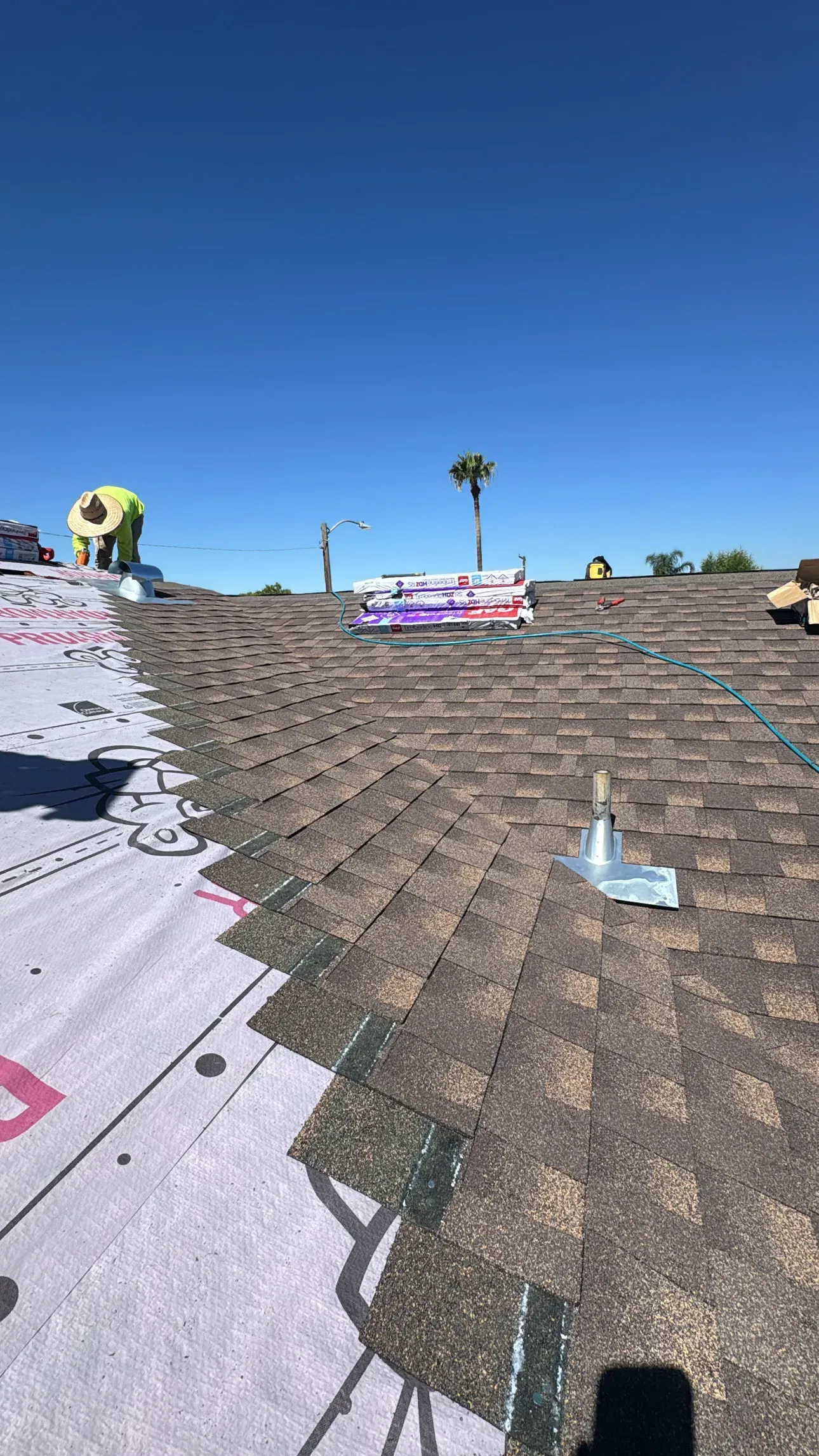 Roofers installing brown shingles on a roof under a clear, blue sky.