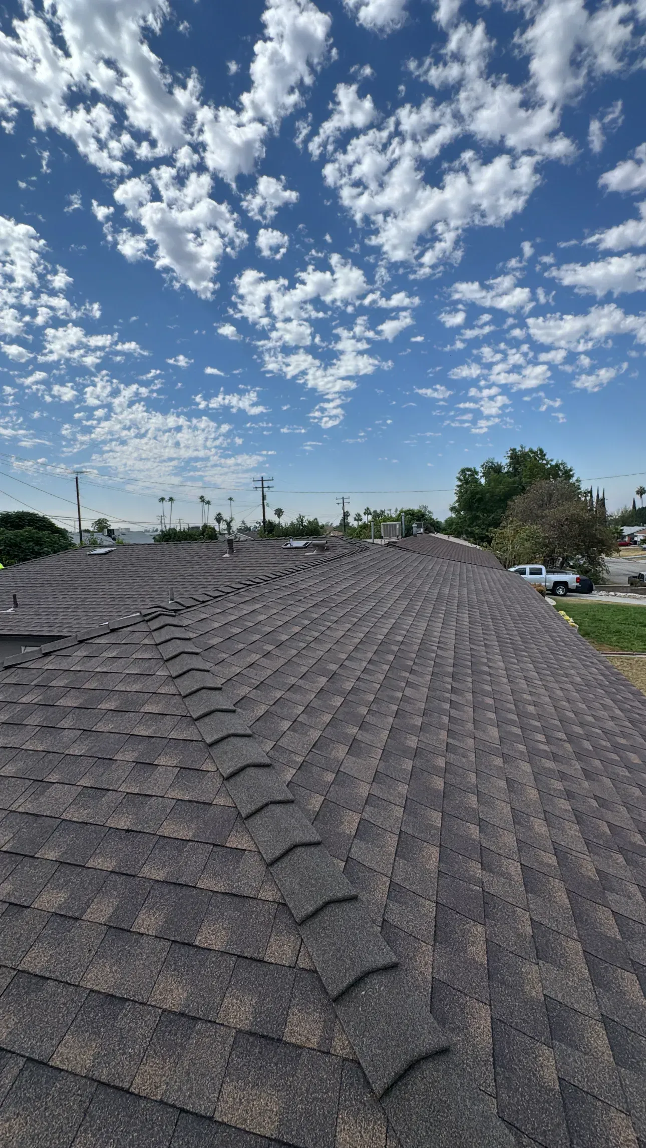 View of a dark gray asphalt shingle roof with blue sky and clouds.