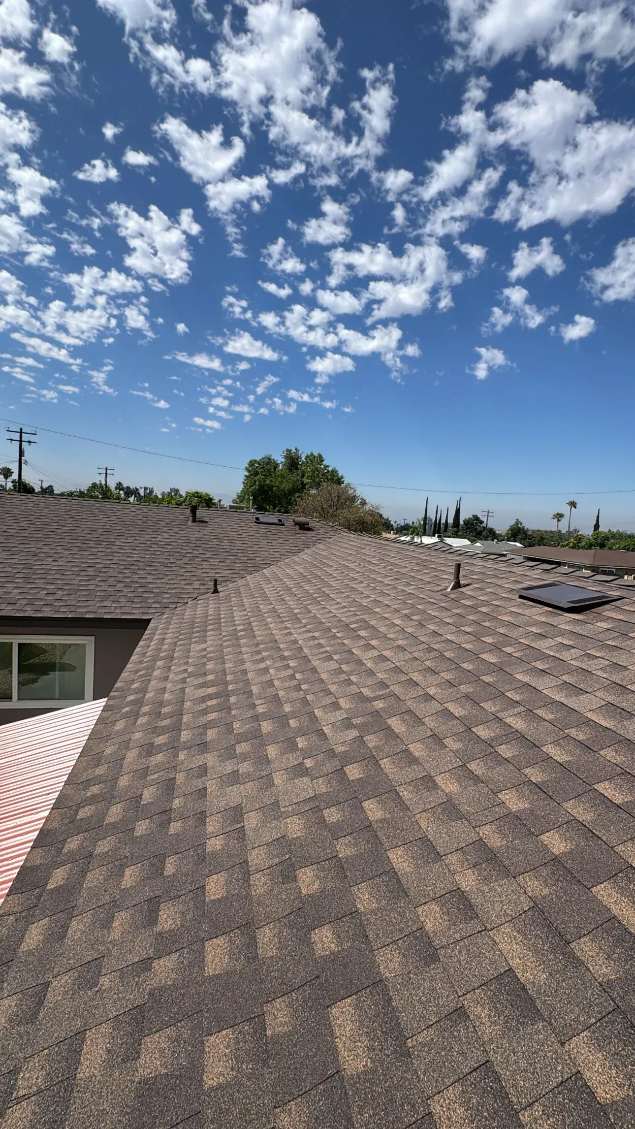 Brown shingle roof under a blue sky with scattered white clouds.