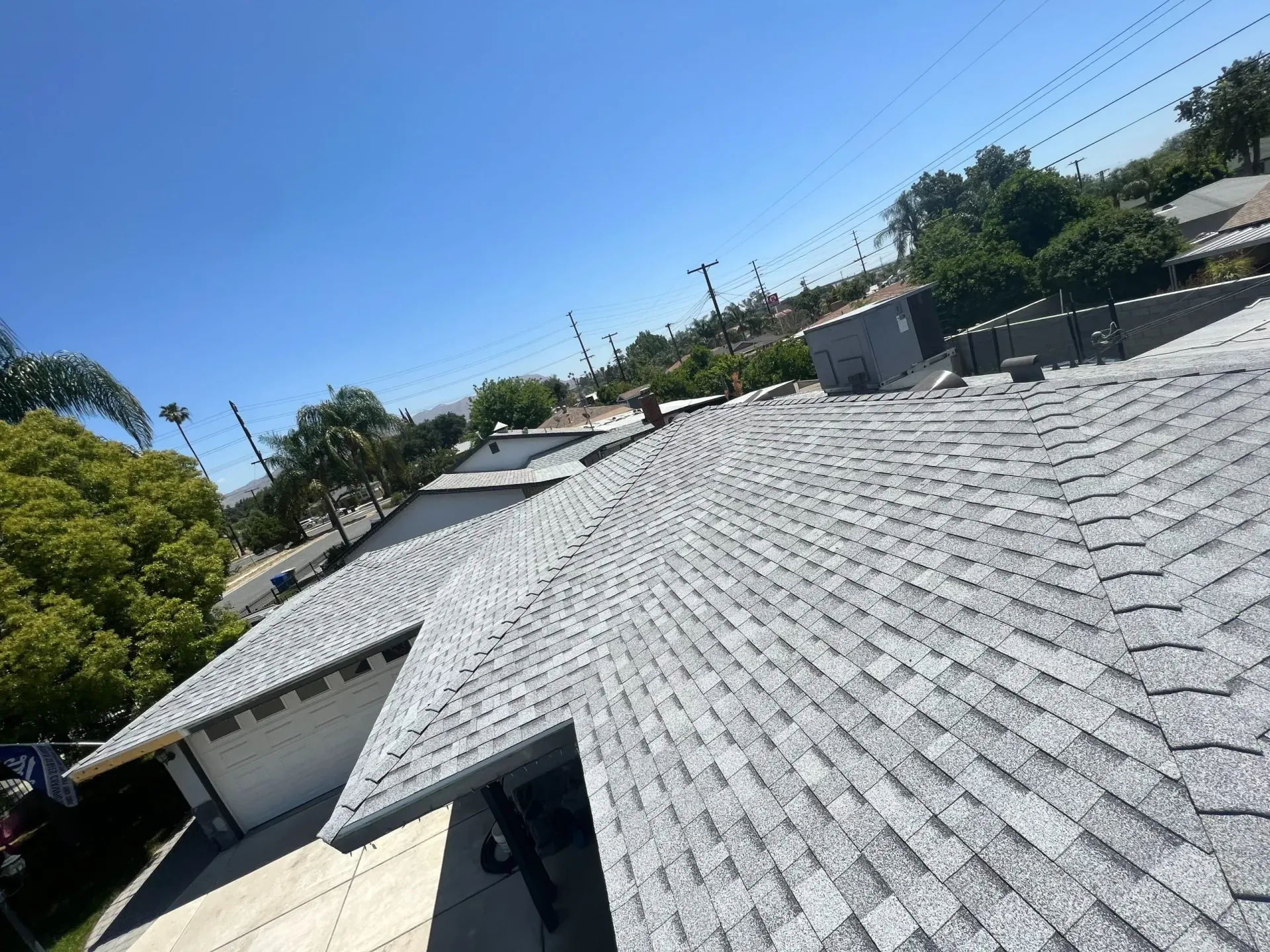Gray shingle roof on a house under a clear blue sky, with trees in the background.