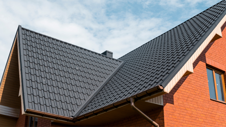 A two-story brick house with a dark gray, tiled roof against a blue sky.