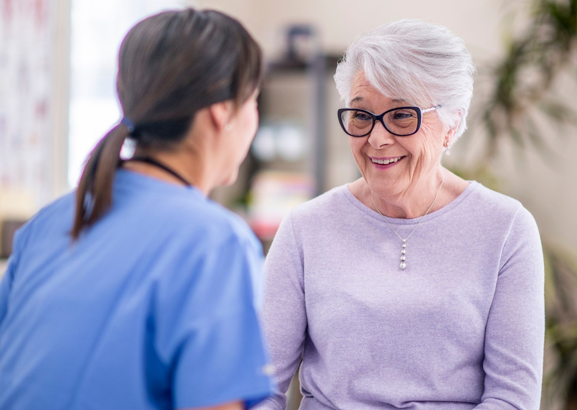 An elderly woman is smiling while talking to a nurse.