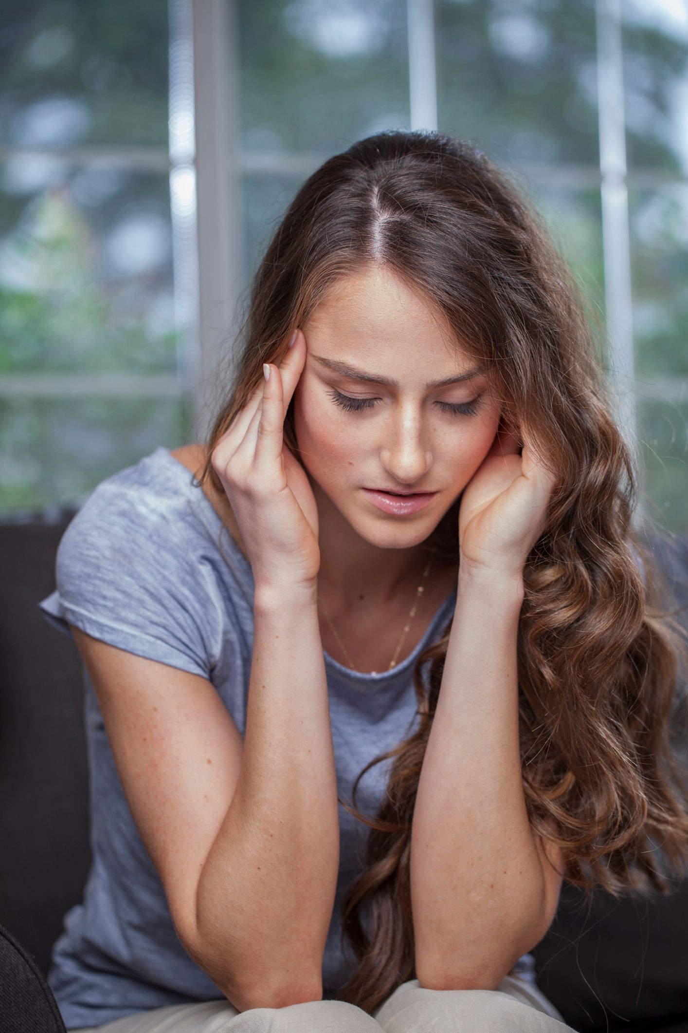 A woman is sitting on a couch with her hands on her head.