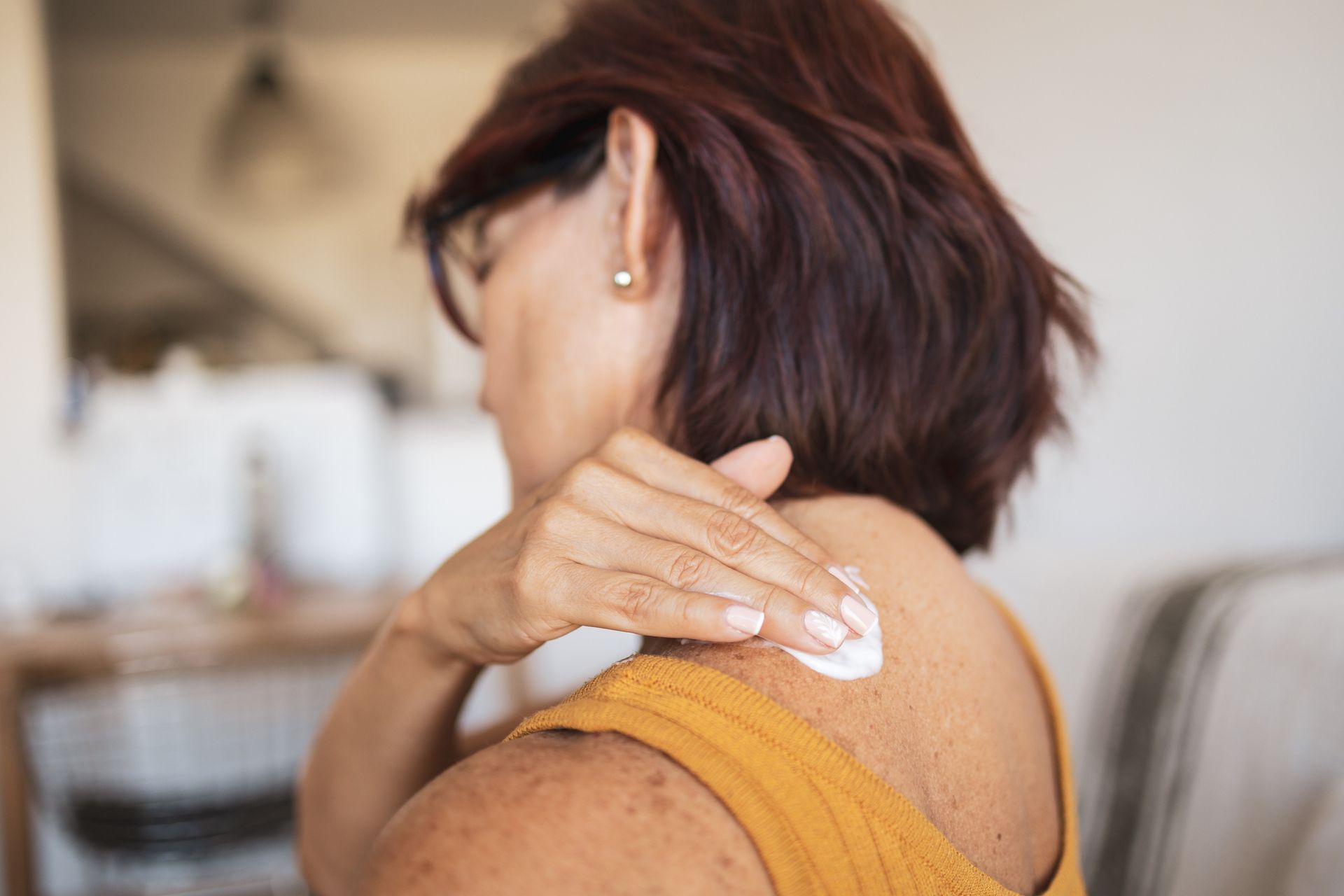 A woman is applying lotion to her back.