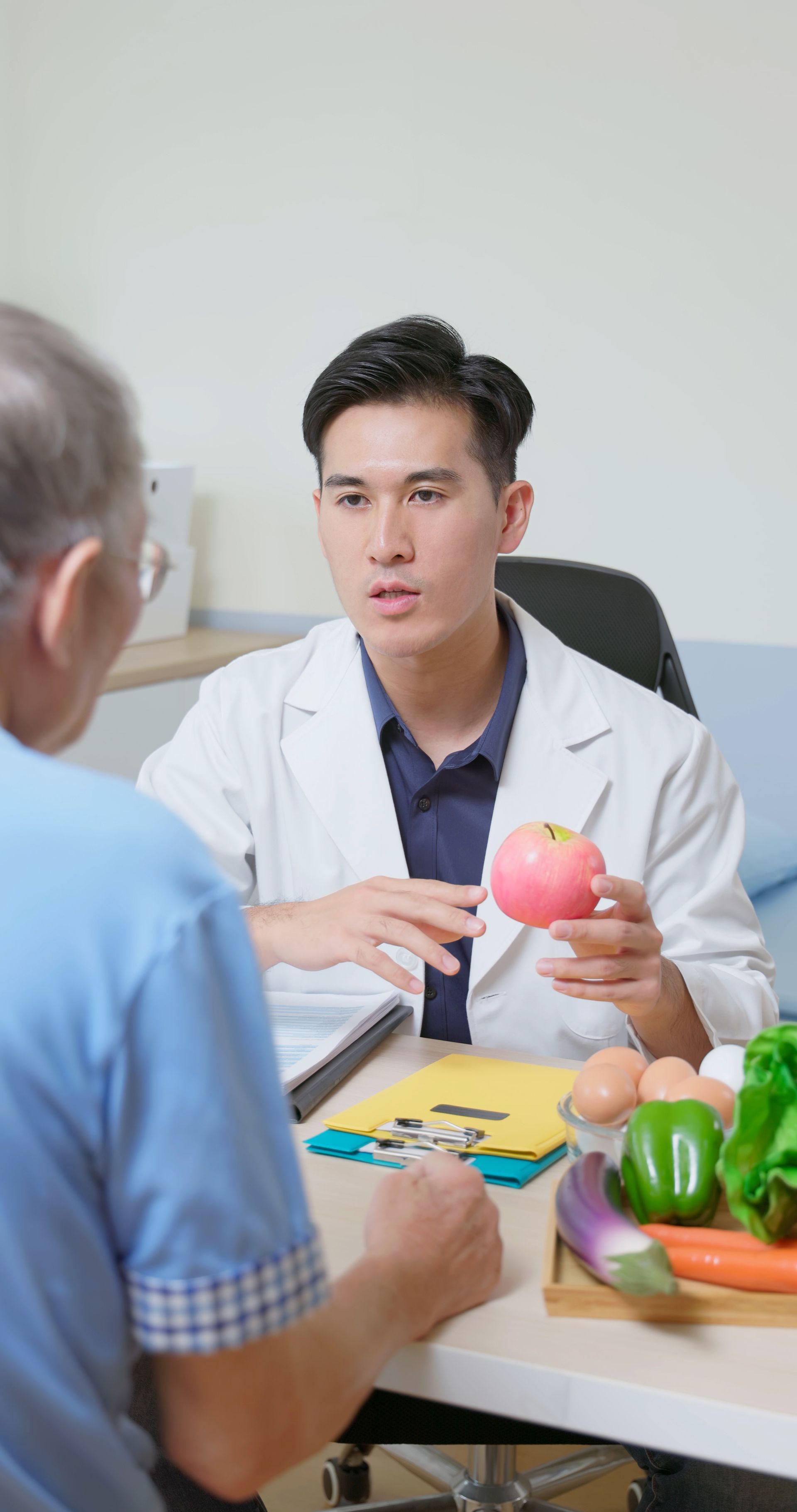 A doctor is talking to a patient while holding an apple.