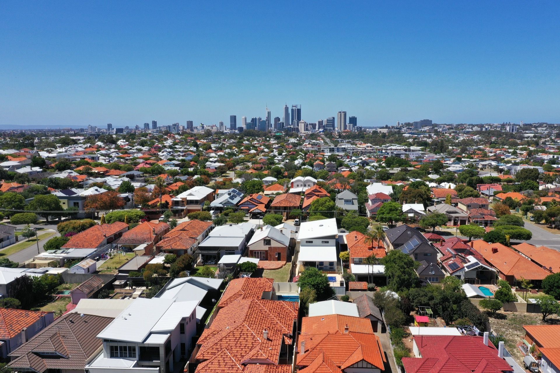 An aerial view of a residential neighborhood with red-tiled roofs, looking toward a distant city skyline under blue sky — Brightside Buyers Agency in Dundas, NSW