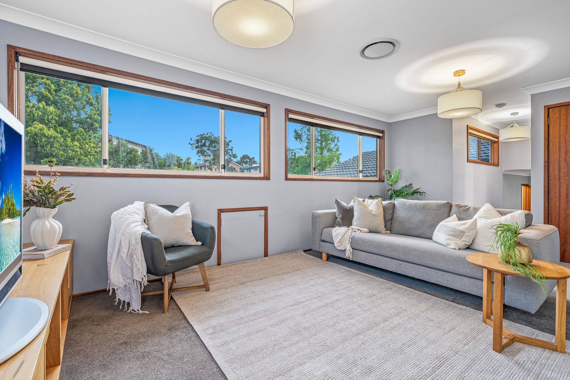 A living room with light grey walls, a grey sofa, a matching armchair, a textured rug, and large windows with wooden frames — Brightside Buyers Agency in Dundas, NSW