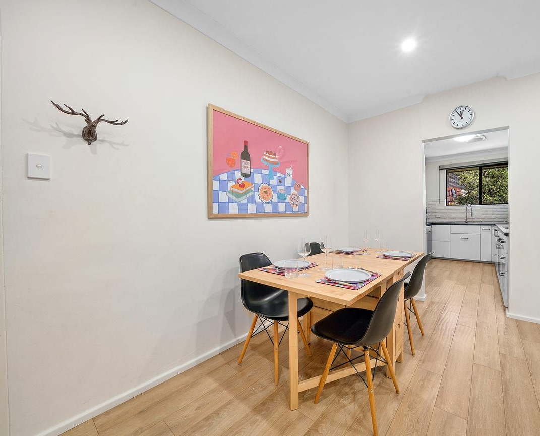 A dining table with four black chairs, a framed pink artwork on the wall, and an antler wall ornament in a bright room — Brightside Buyers Agency in Dundas, NSW