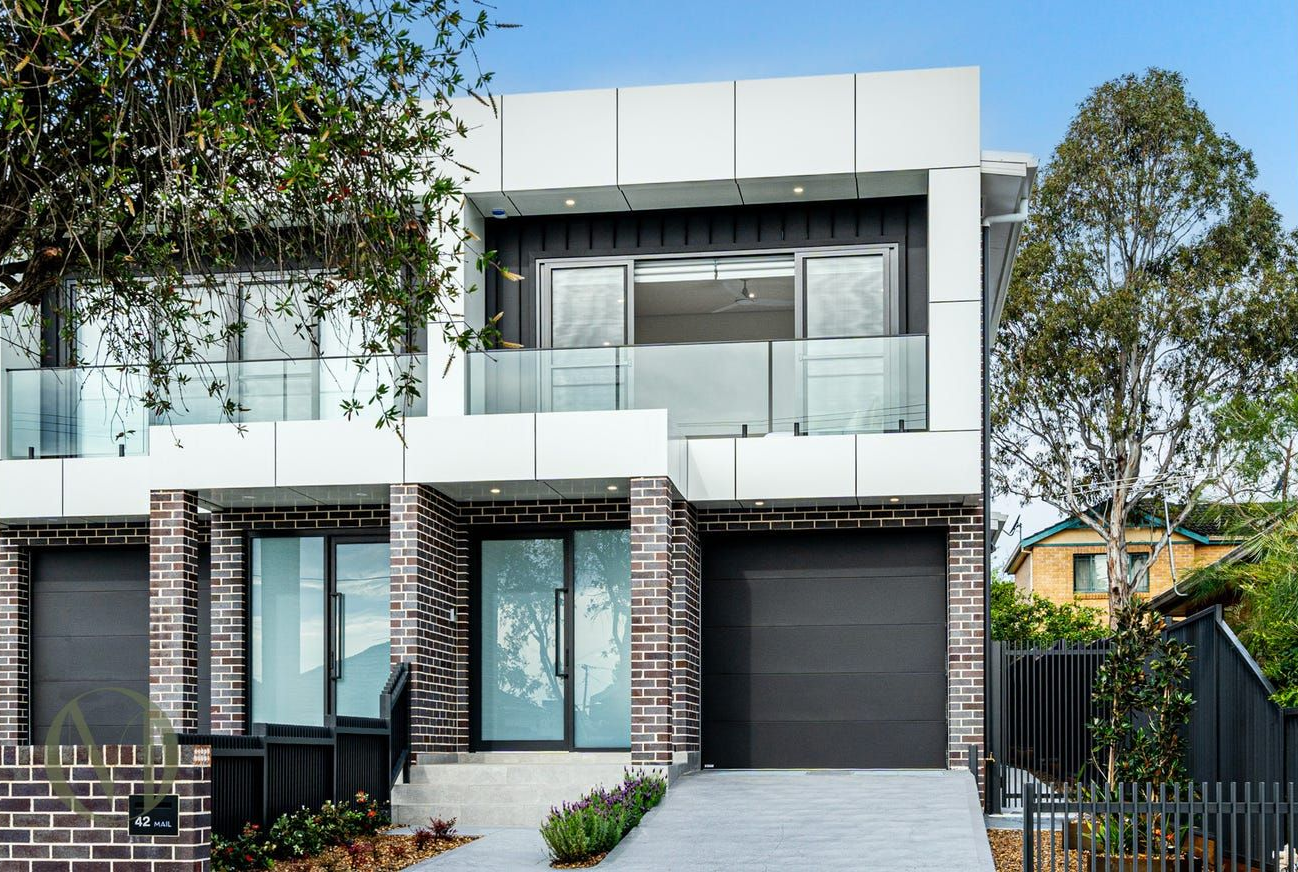 A two-story modern house with a white facade, brick accents, a balcony, and a dark garage door, set under a blue sky  — Brightside Buyers Agency in Dundas, NSW