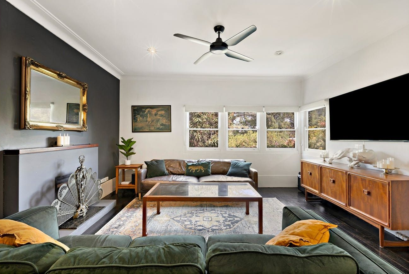 A cozy living room with a green sofa, coffee table, fireplace with a large mirror, and a wall-mounted TV on a wood console — Brightside Buyers Agency in The Hills Shire, NSW