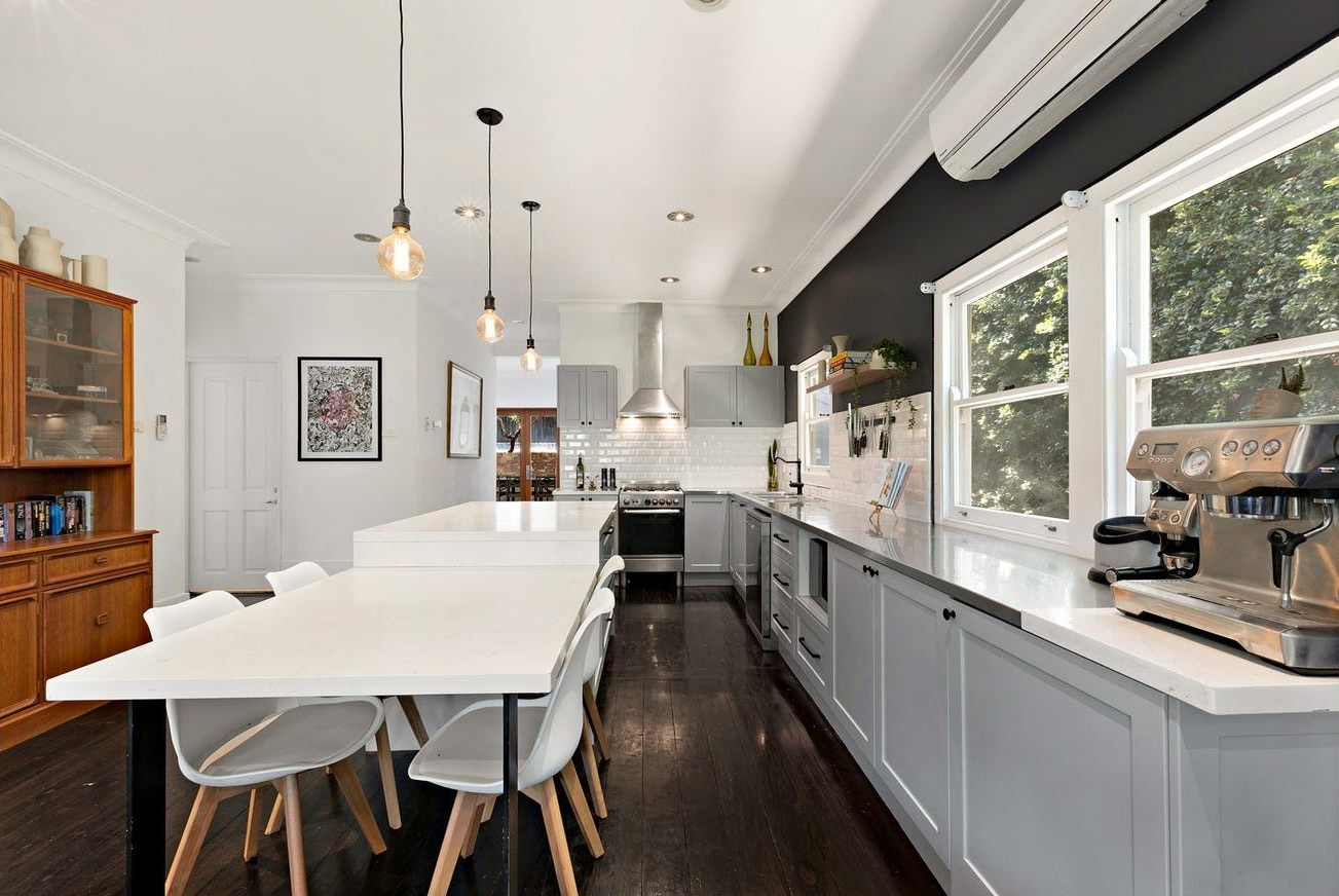 A bright, modern kitchen features light grey cabinets, a white island, white chairs, and dark wood flooring  — Brightside Buyers Agency in Dundas, NSW