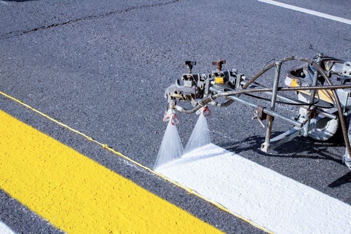 A machine is spraying yellow and white paint on a road.