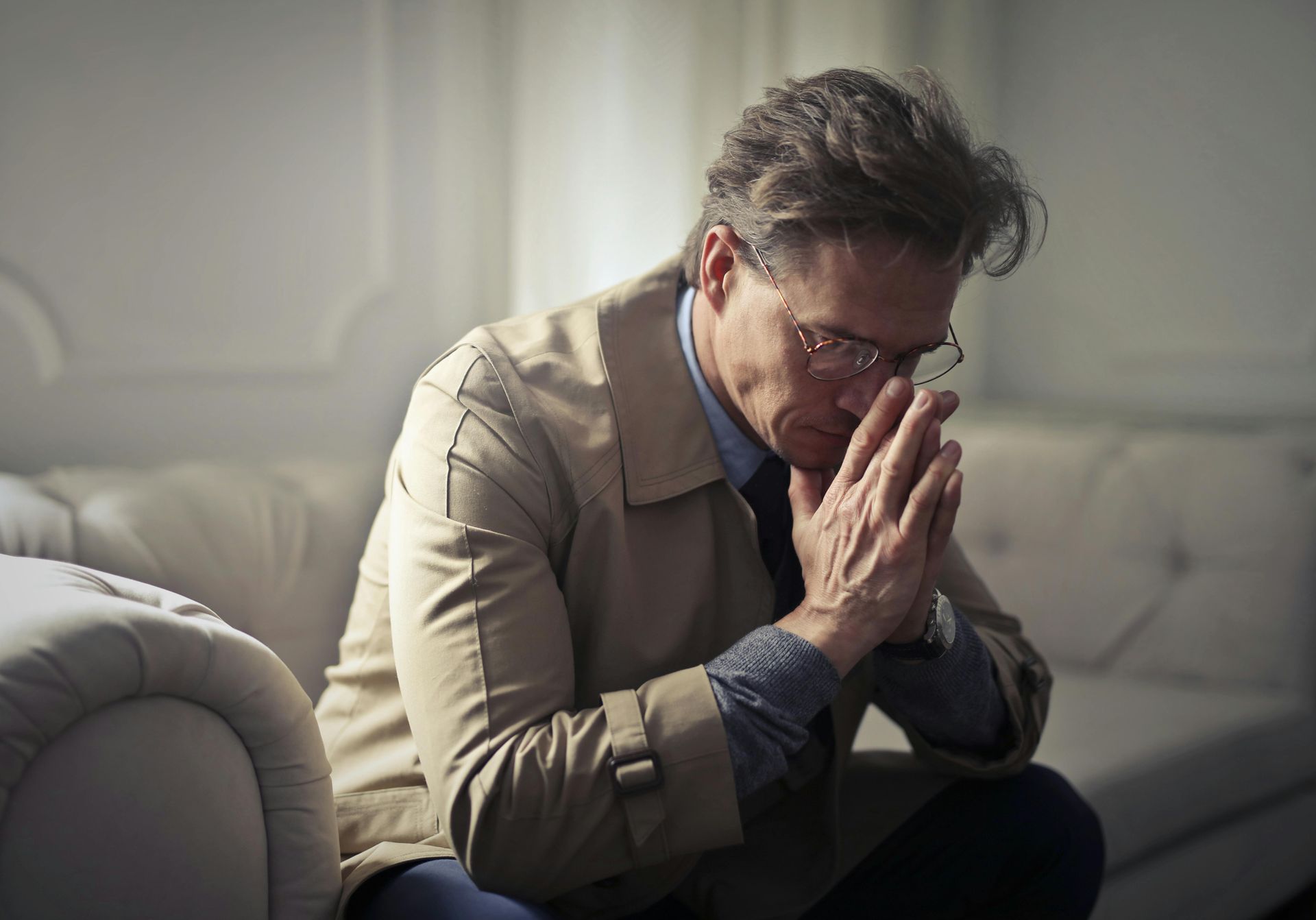 A man is sitting on a couch with his hands folded in prayer.