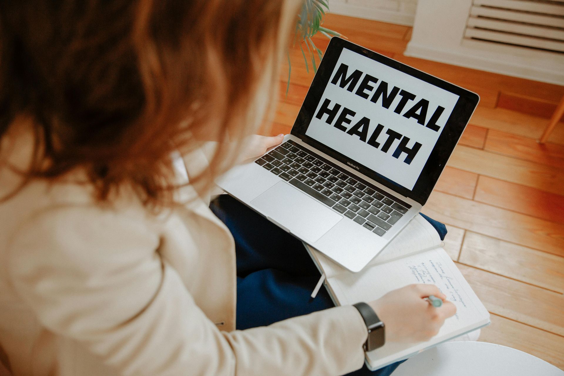 A woman is sitting in front of a laptop computer with the words mental health on the screen.