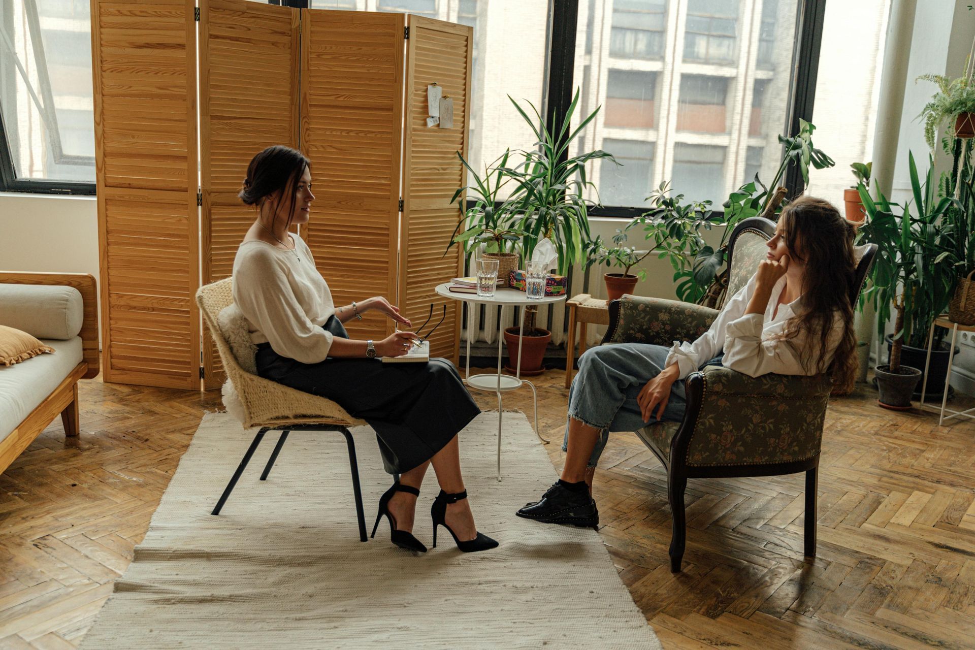 A woman is sitting in a chair talking to another woman in a living room.