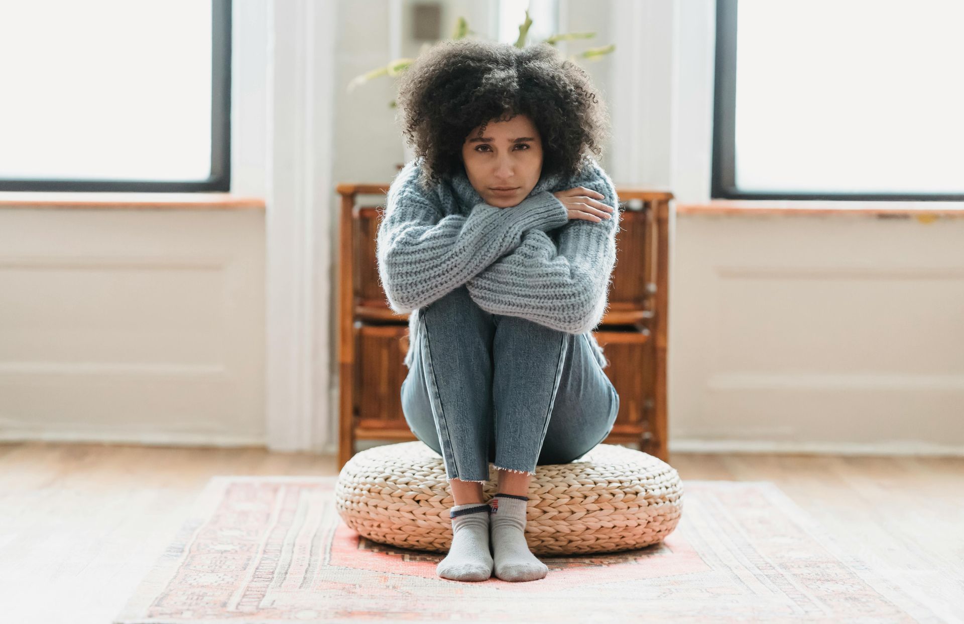 A woman is sitting on a pillow on the floor in a living room.