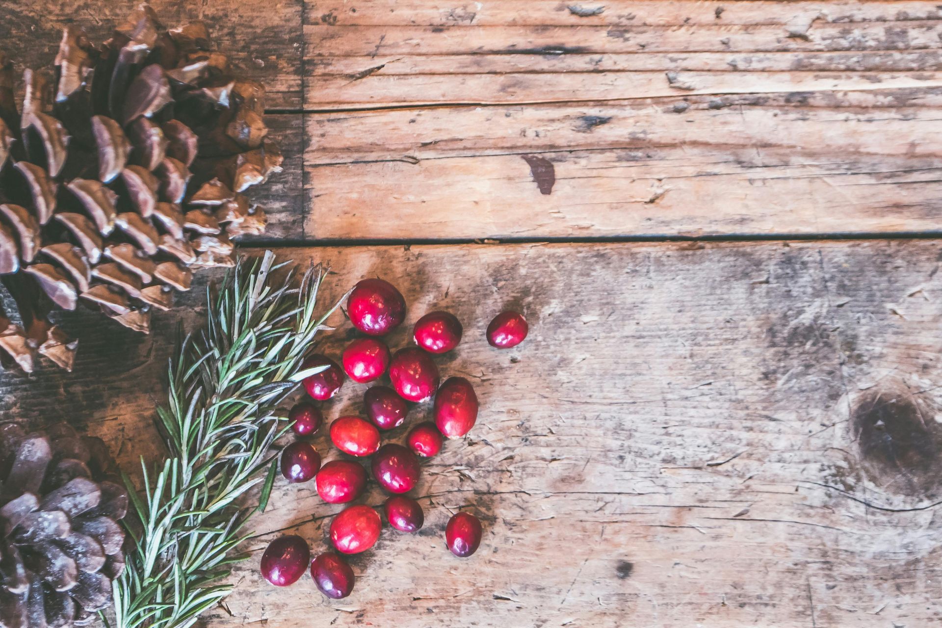 There are pine cones and cranberries on the wooden table.