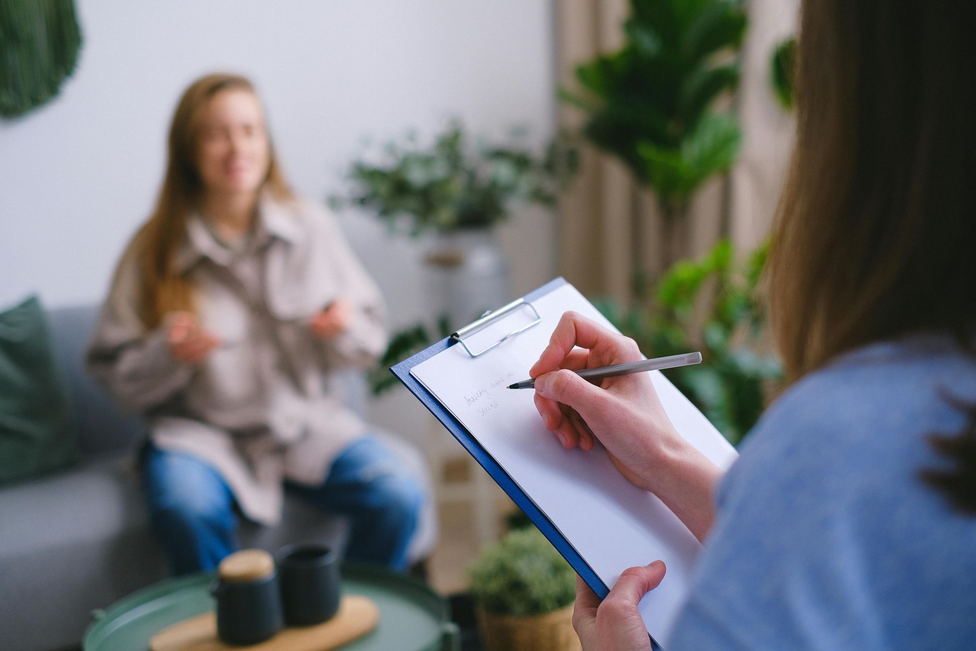 A woman is sitting on a couch while a woman writes on a clipboard.