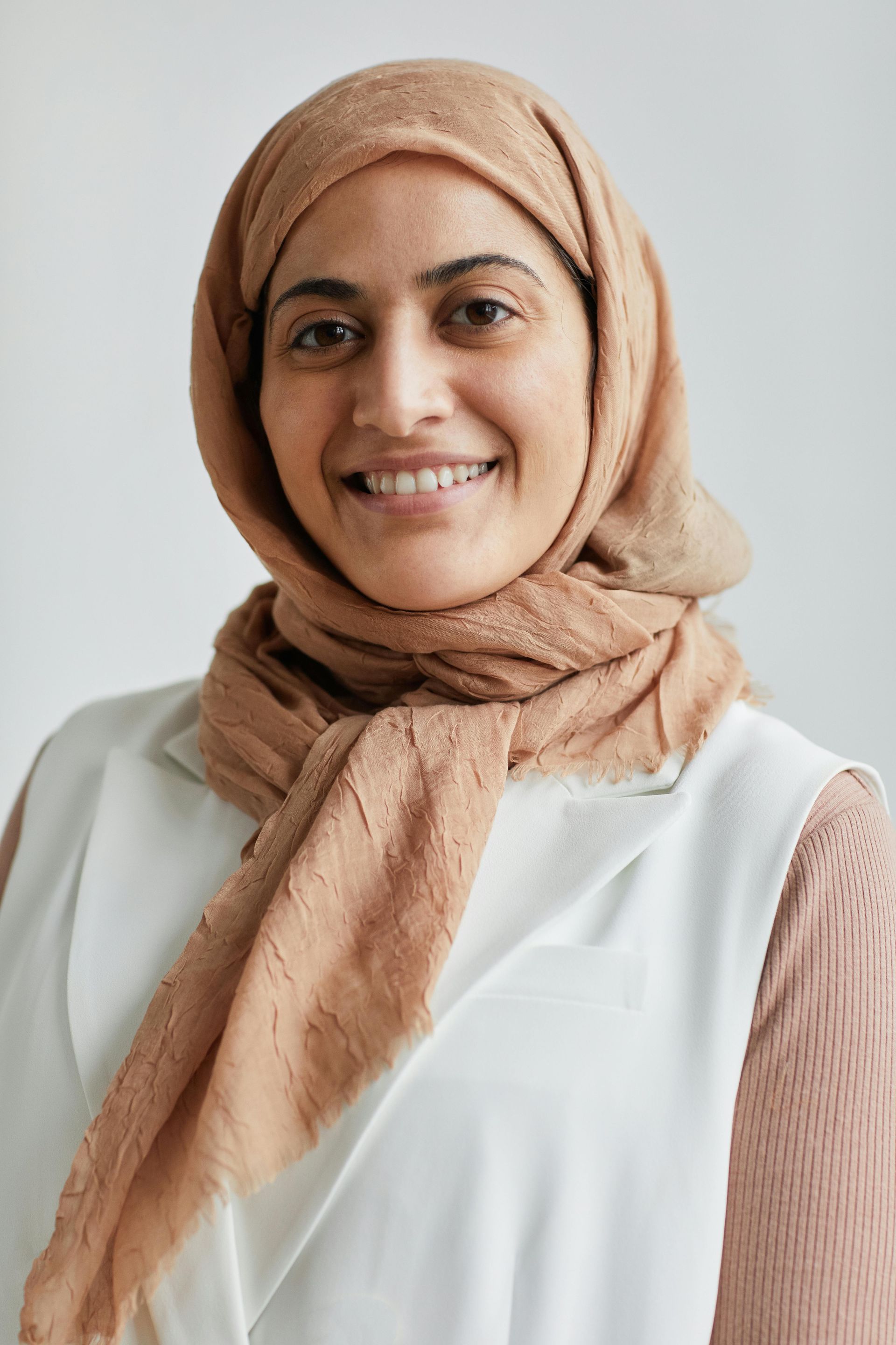 A woman wearing a hijab and a scarf is smiling for the camera.