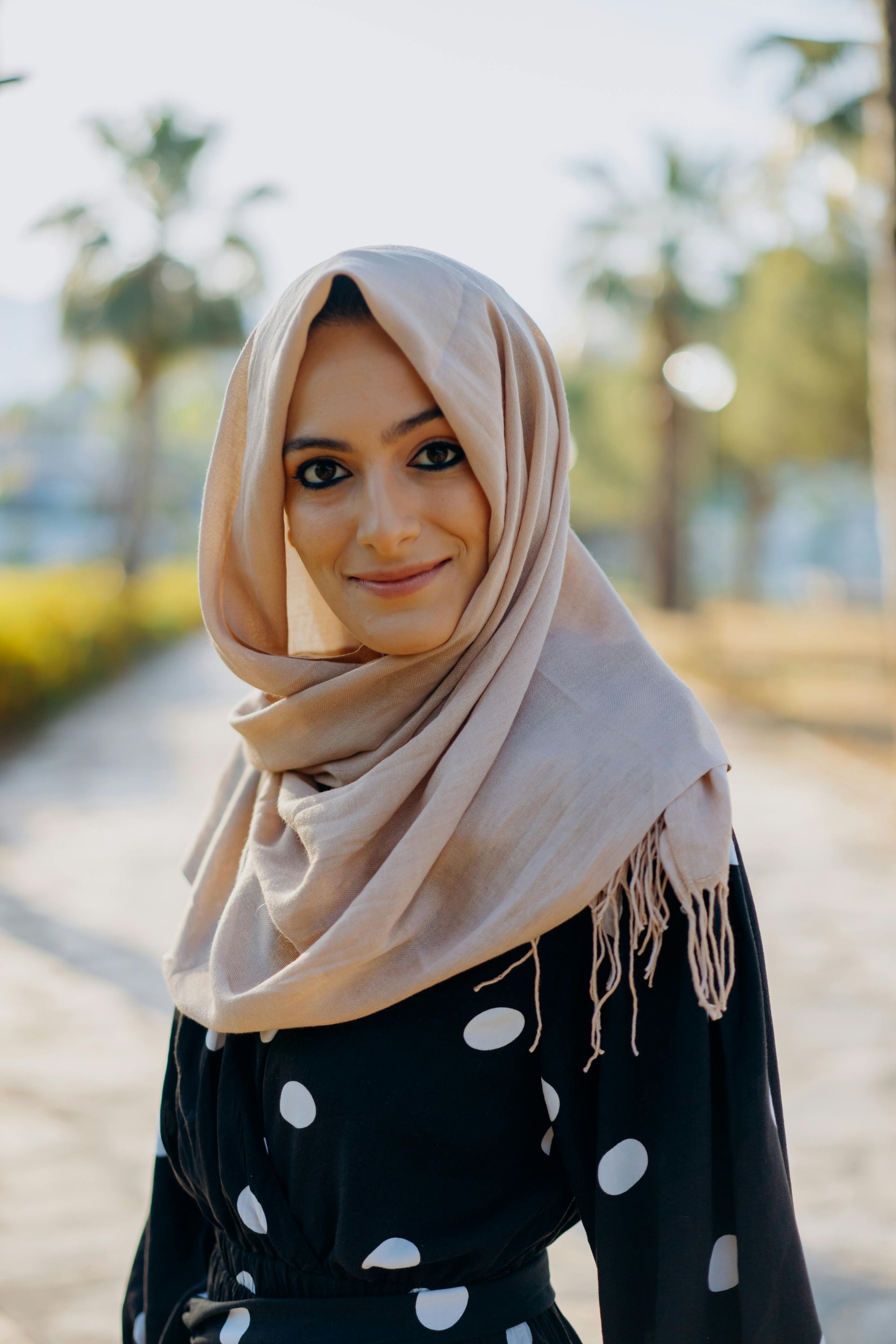 A woman wearing a hijab and a polka dot dress is standing on a sidewalk.