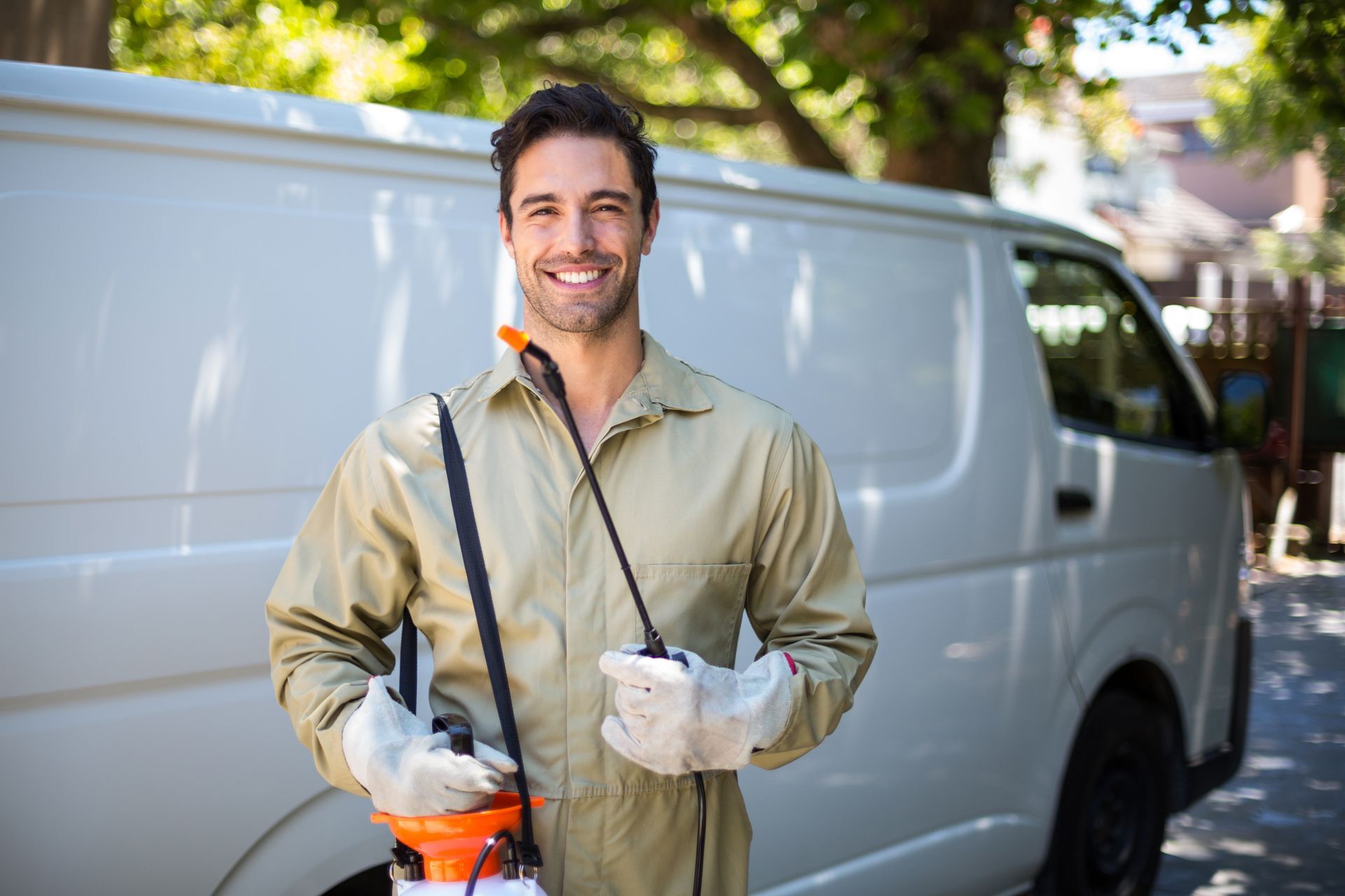 Person holding a garden sprayer stands in front of a white service van outdoors.