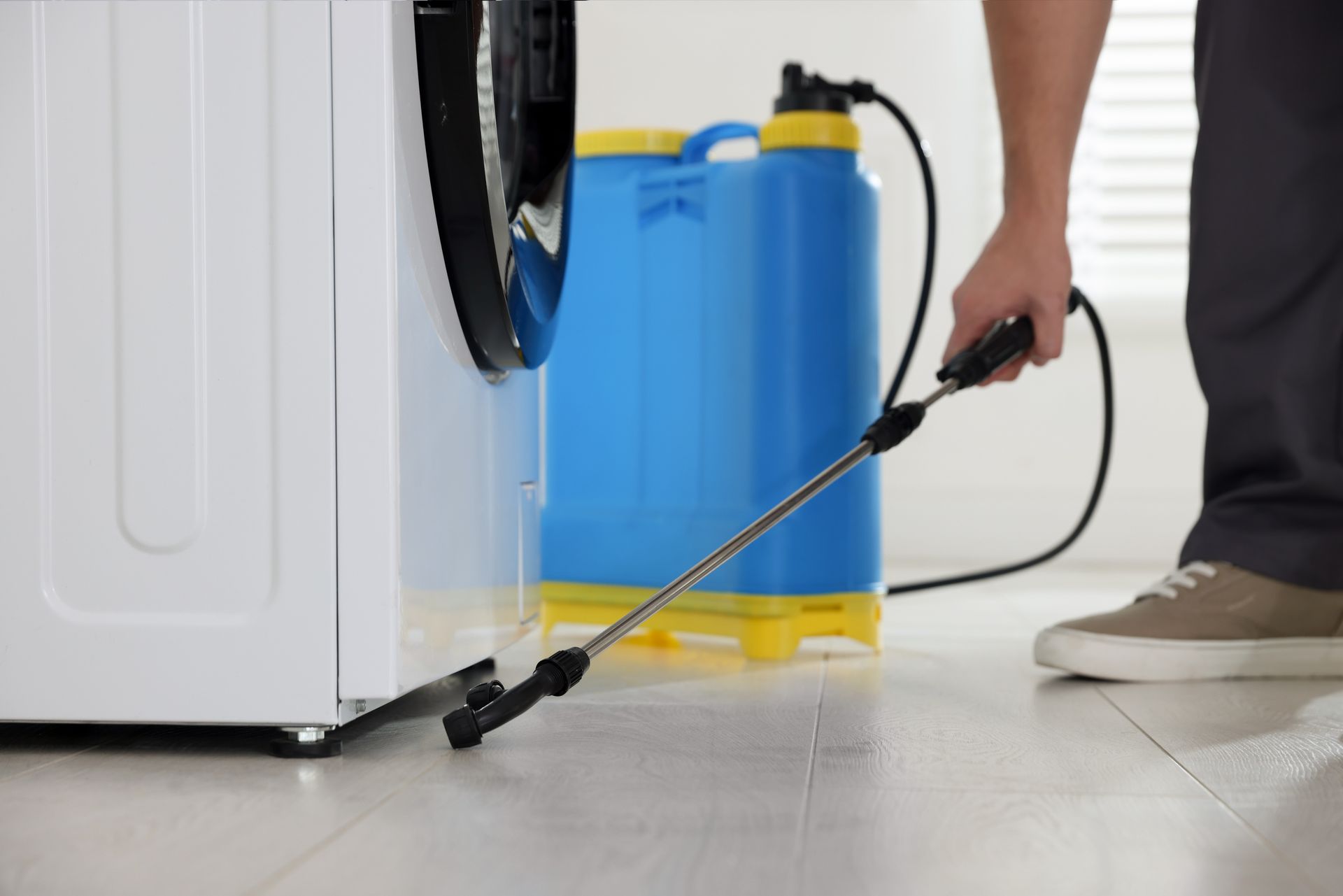 Pest control technician spraying treatment around a household appliance with a backpack sprayer. Pest control technician spraying treatment around a household appliance with a backpack sprayer.