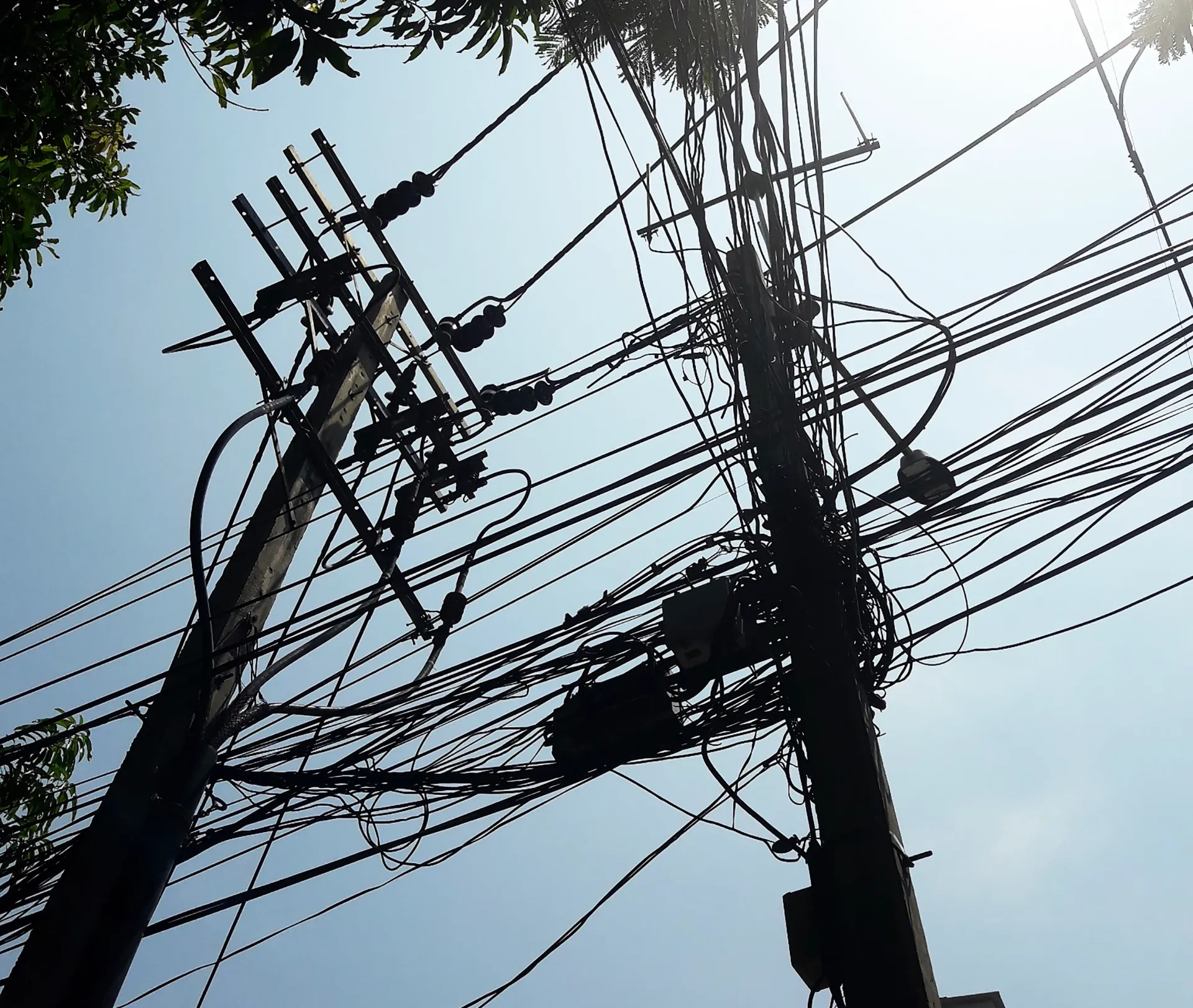 Utility poles tangled with many overhead power lines against a bright sky
