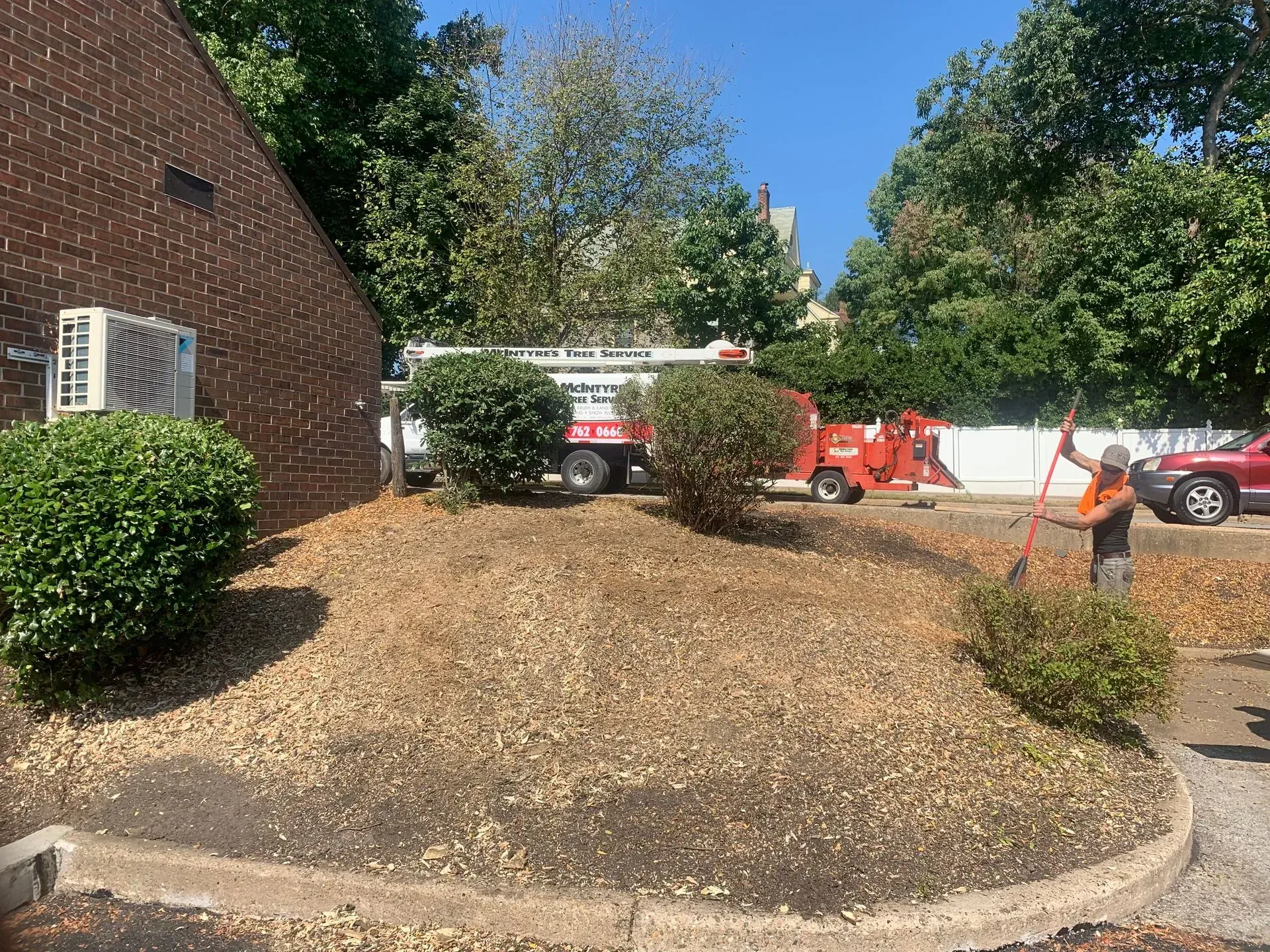 A man is raking leaves in front of a brick building.