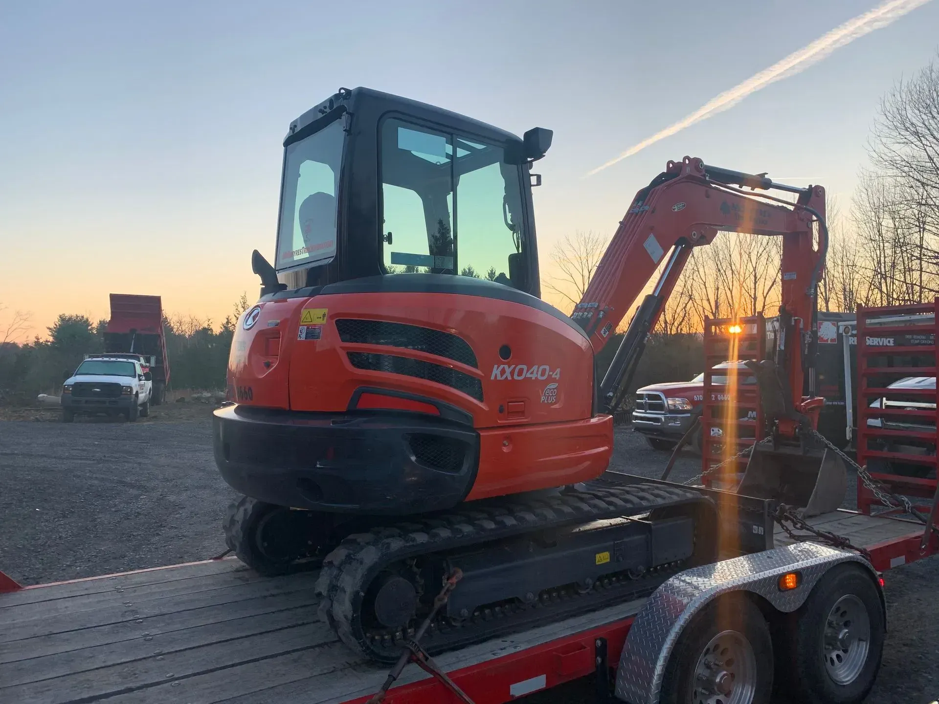 A small orange excavator is sitting on top of a trailer.