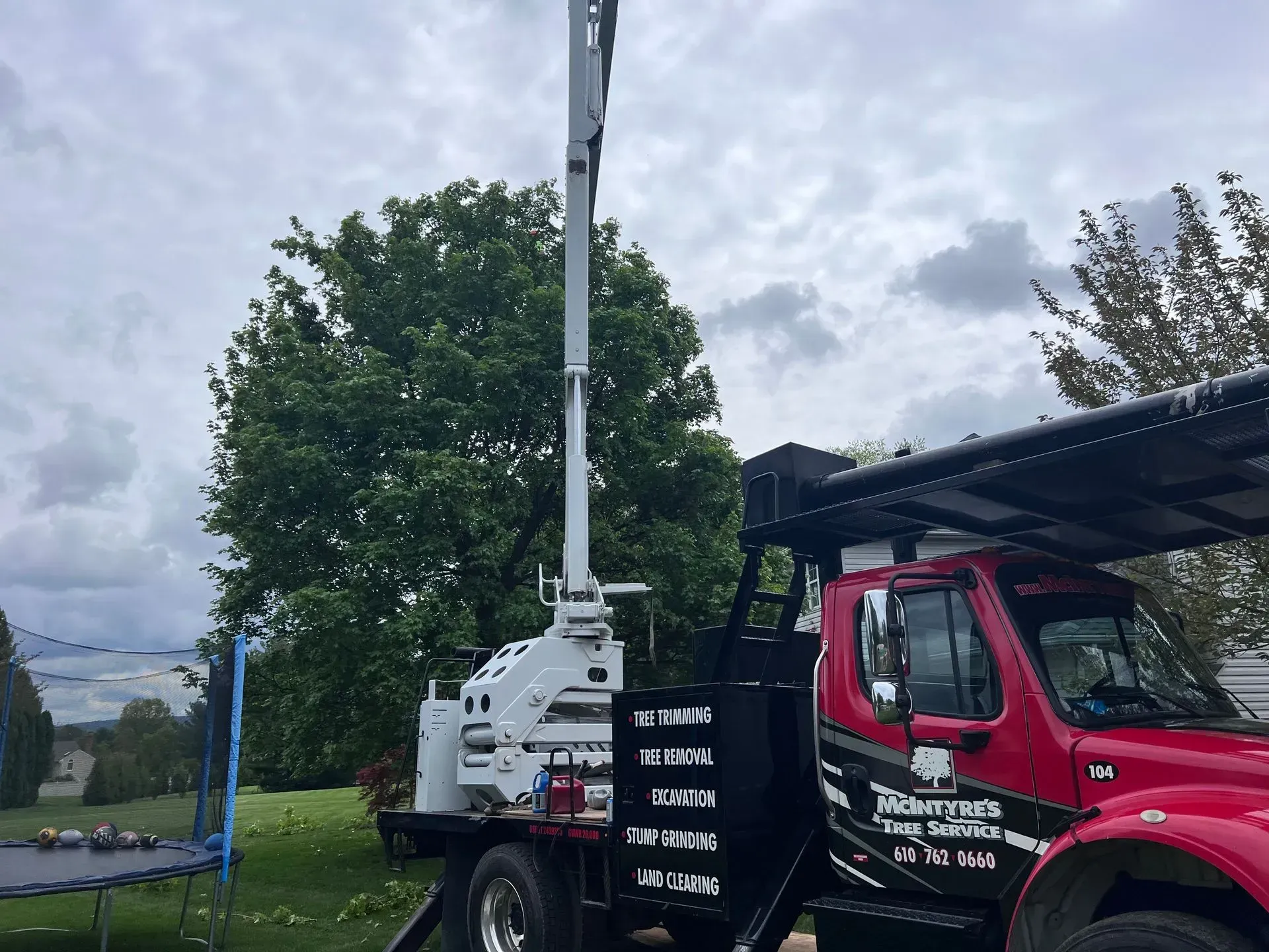 A red truck with a crane on the back is parked in front of a trampoline.