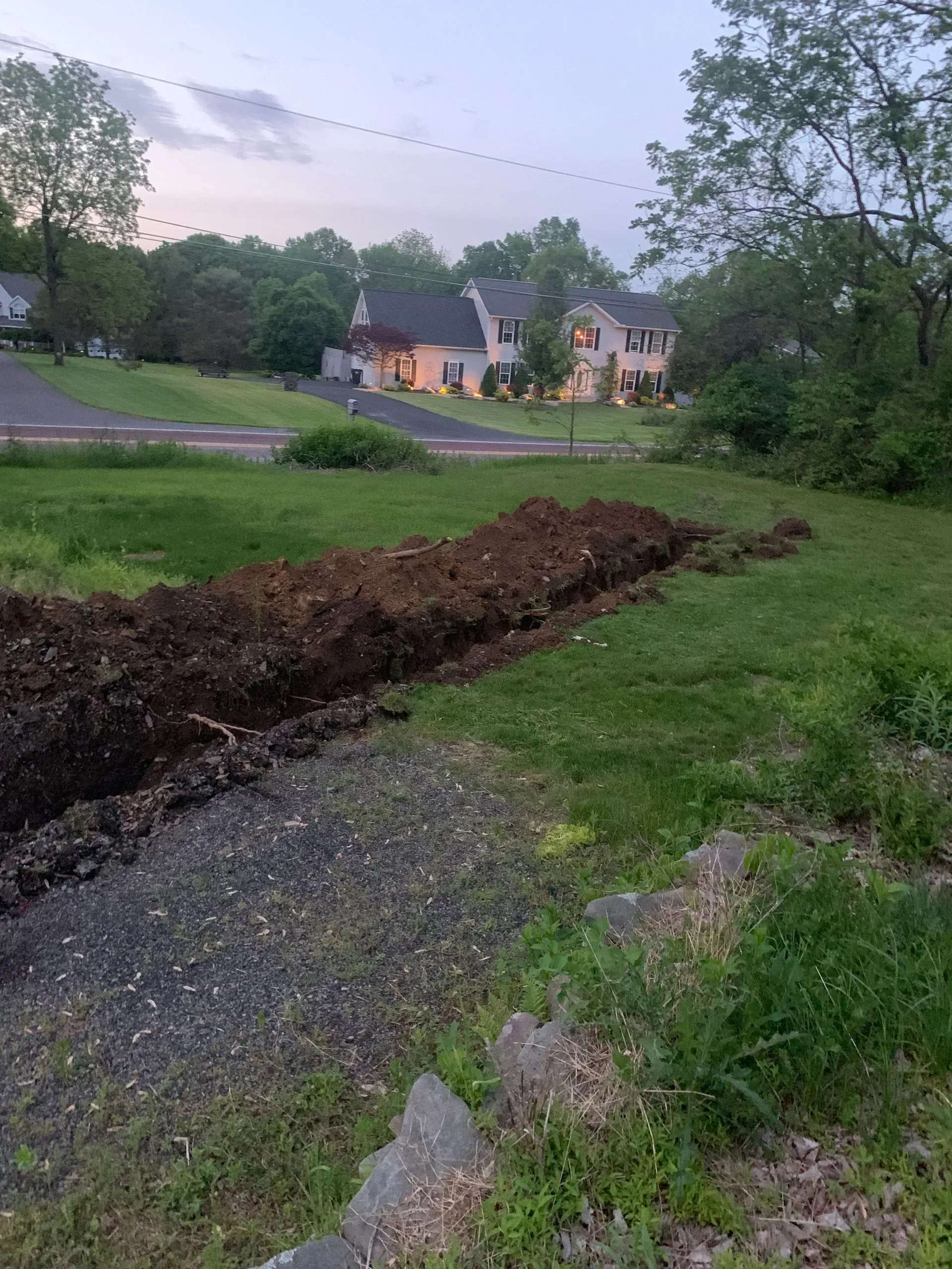 A large pile of dirt is in the middle of a grassy field in front of a house.