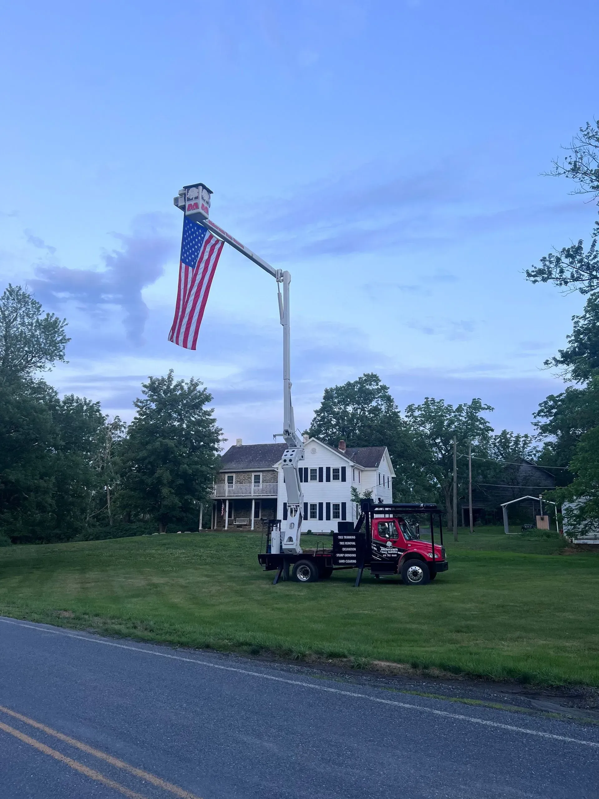 A red truck is parked on the side of the road next to a pole with an american flag on it.