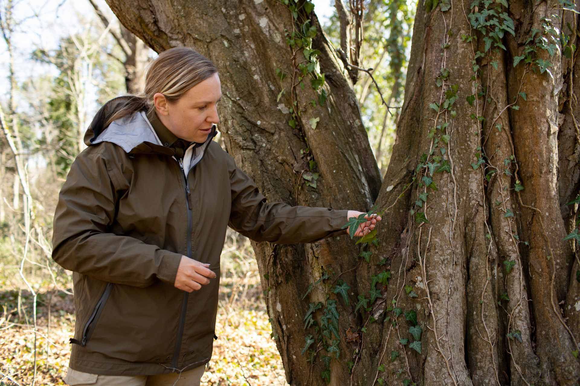 A woman in a brown jacket is standing next to a tree.