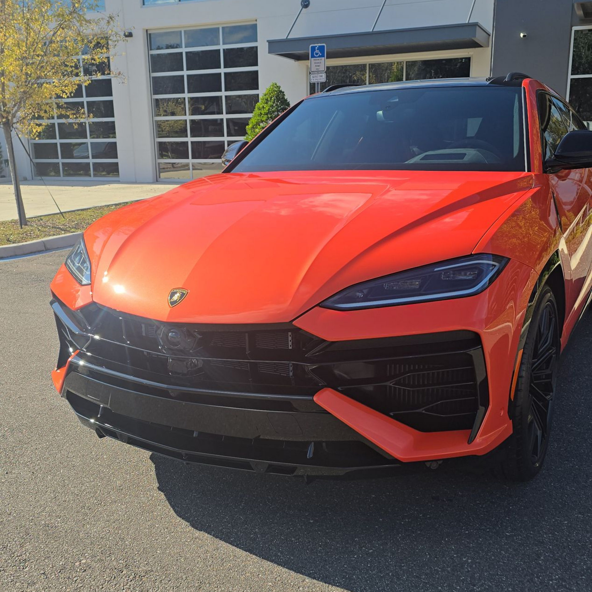 Bright orange Lamborghini Urus SUV parked in front of a building with a glass garage door.