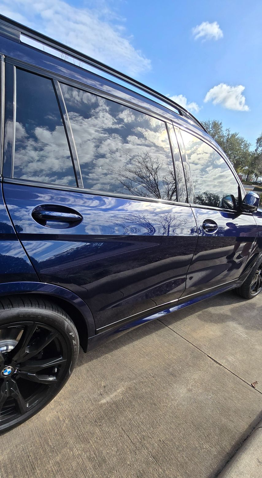 Dark blue SUV with tinted windows, parked on a concrete surface, reflecting clouds.